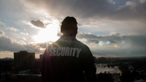 A black male security guard in uniform watching over the street from the high floor.